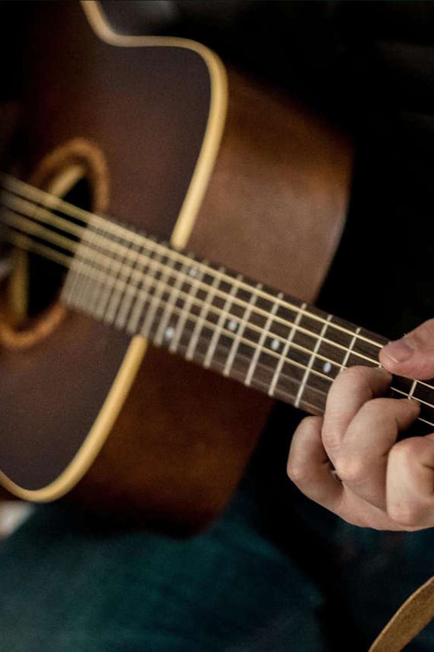 Nahaufnahme einer Person, die auf einer braunen akustischen Gitarre spielt, mit Fokus auf den Griffbrett und den Fingern der linken Hand