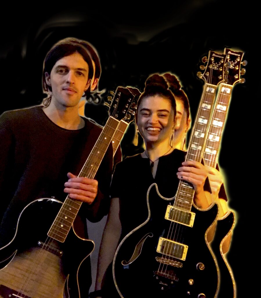 Zwei Musiker mit Elektrogitarren vor dunklem Hintergrund, plötzliches Doppelbild durch Lichtspuren, der Mann links hält eine Gitarre mit hellem Holzkorpus, die Frau rechts lächelt und hält eine schwarze Doppelhalsgitarre.