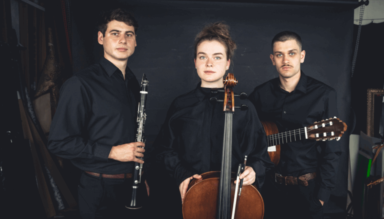 Drei Musiker in schwarzer Kleidung vor schwarzem Hintergrund, links ein Mann mit Klarinette, in der Mitte eine Frau mit Cello und Bogen, rechts ein Mann mit akustischer Gitarre