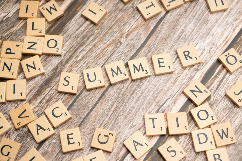 Holzbuchstaben auf einem Holztisch, die das Wort SUMMER bilden, umgeben von verstreuten Buchstabensteinen. Für den Sommer sollten Sie Musiker mit langer Vorlaufzeit buchen.