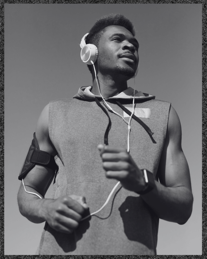 Musik und Sport sind untrennbar: Schwarz-weiß-Foto eines sportlichen Mannes mit Kopfhörern, der in einem ärmellosen Hoodie joggt und nach oben schaut, vor klarem Himmel.