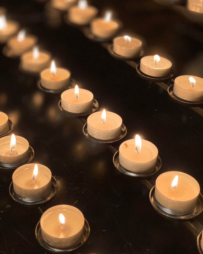 Mehrere brennende Teelichter in Metallhalterungen auf einer schwarzen Oberfläche, unscharfer Hintergrund mit weiteren Kerzenlichtern.