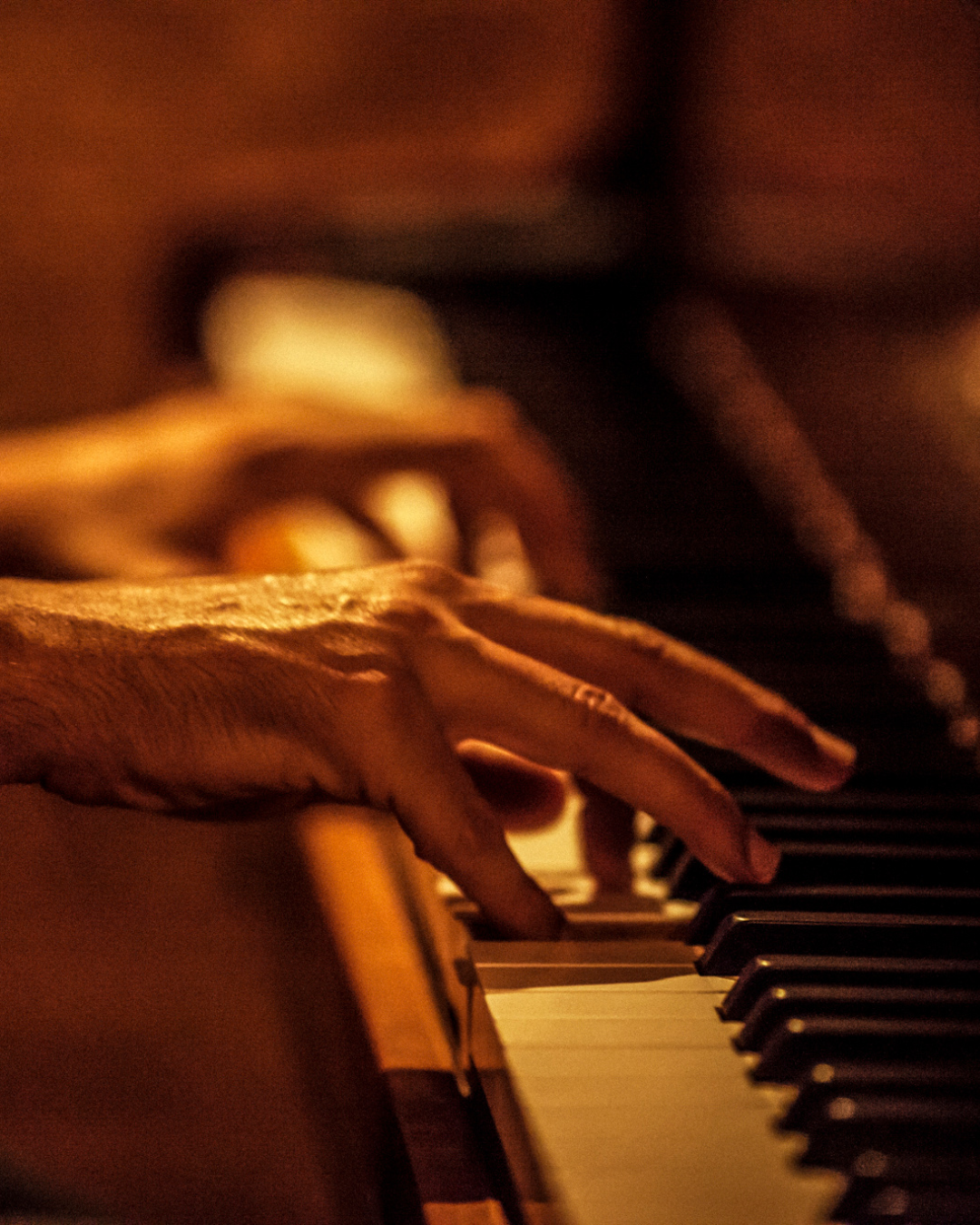 Moderner Abschiedsmusik live: Hände, die in warmem Licht auf den Tasten eines Klaviers spielen