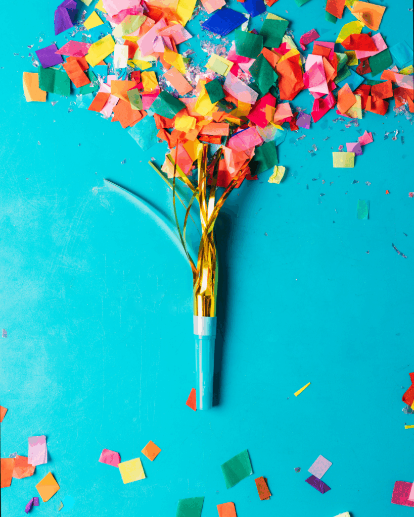 Konfetti-Popper mit goldenen Bänder und farbigem Papierkonfetti auf blauem Hintergrund verteilt