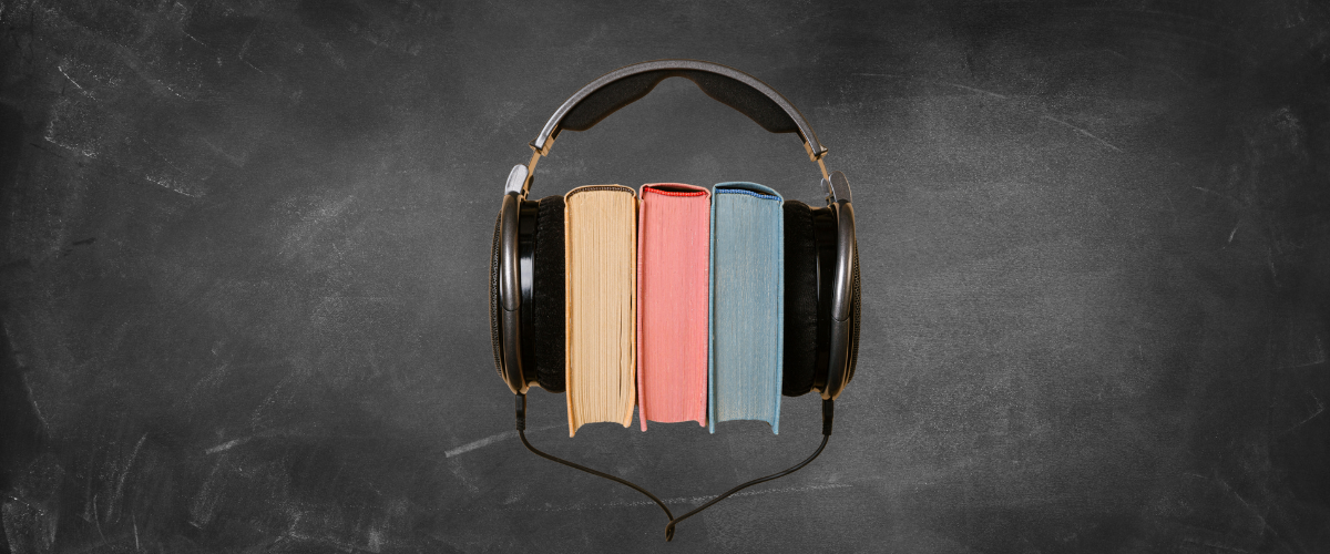 Symbolbild für Lernen mit Musik: Drei Bücher in Gelb, Rot und Blau, die zwischen schwarzen Kopfhörern auf einem dunklen Hintergrund stehen und das Konzept des Hörbuchs symbolisieren