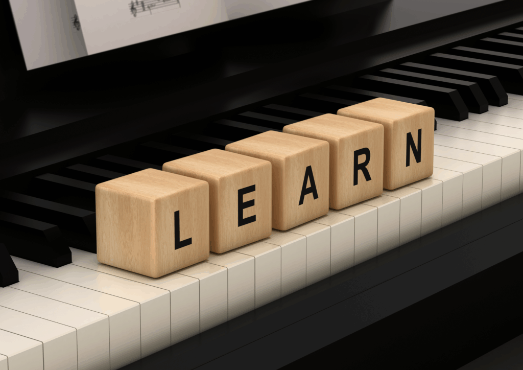 Lernen mit Musik – Klaviertasten mit Holzbuchstaben LEARN. Holzwürfel mit den Buchstaben L, E, A, R, N liegen auf den weißen Tasten eines schwarzen Klaviers, im Hintergrund ist Notenblatt sichtbar.