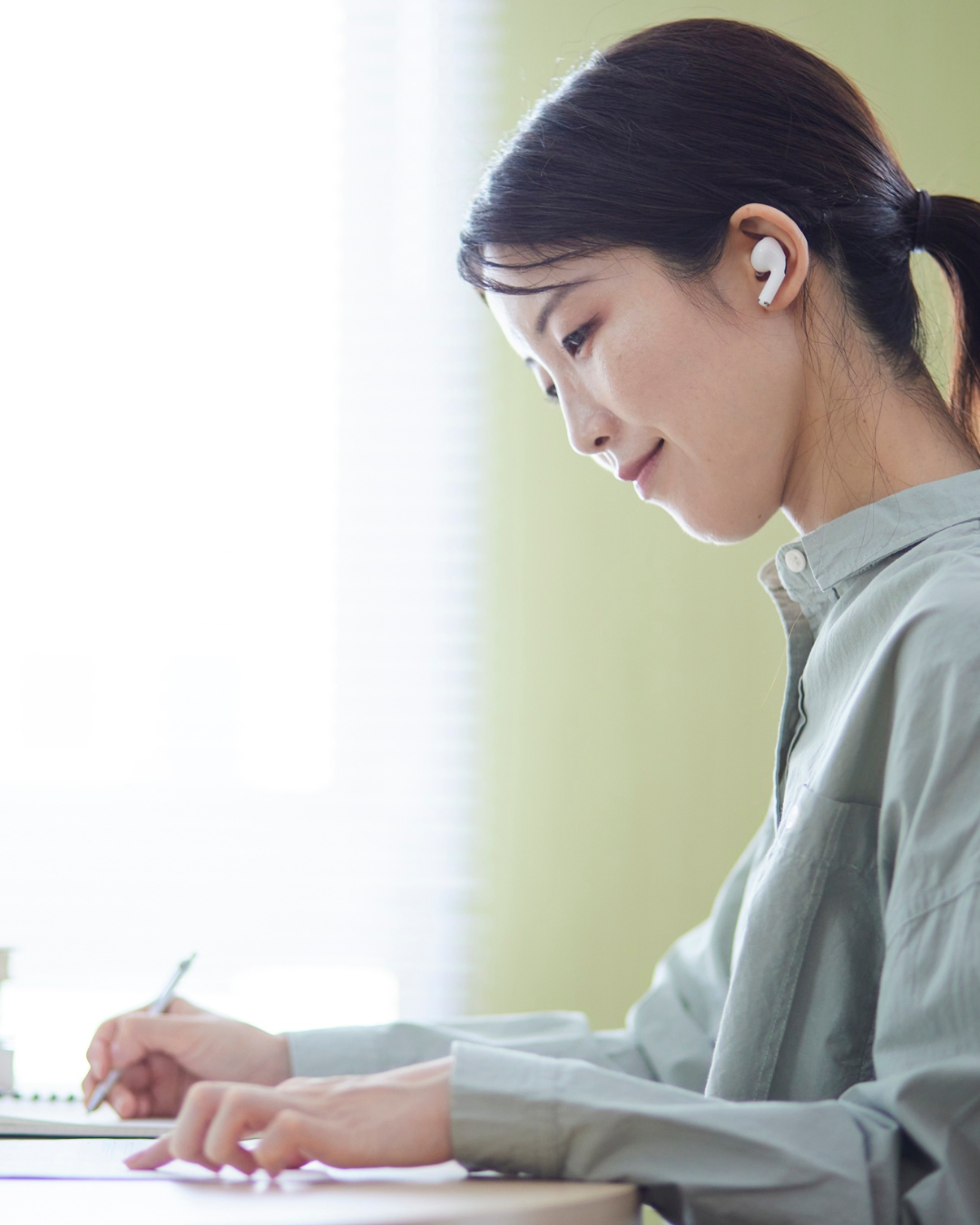 Frau hört beim Lernen Musik über Earbuds und schreibt konzentriert