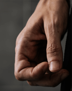 Nahaufnahme einer linken menschlichen Hand mit leicht geballter Faust vor einem unscharfen grauen Hintergrund.