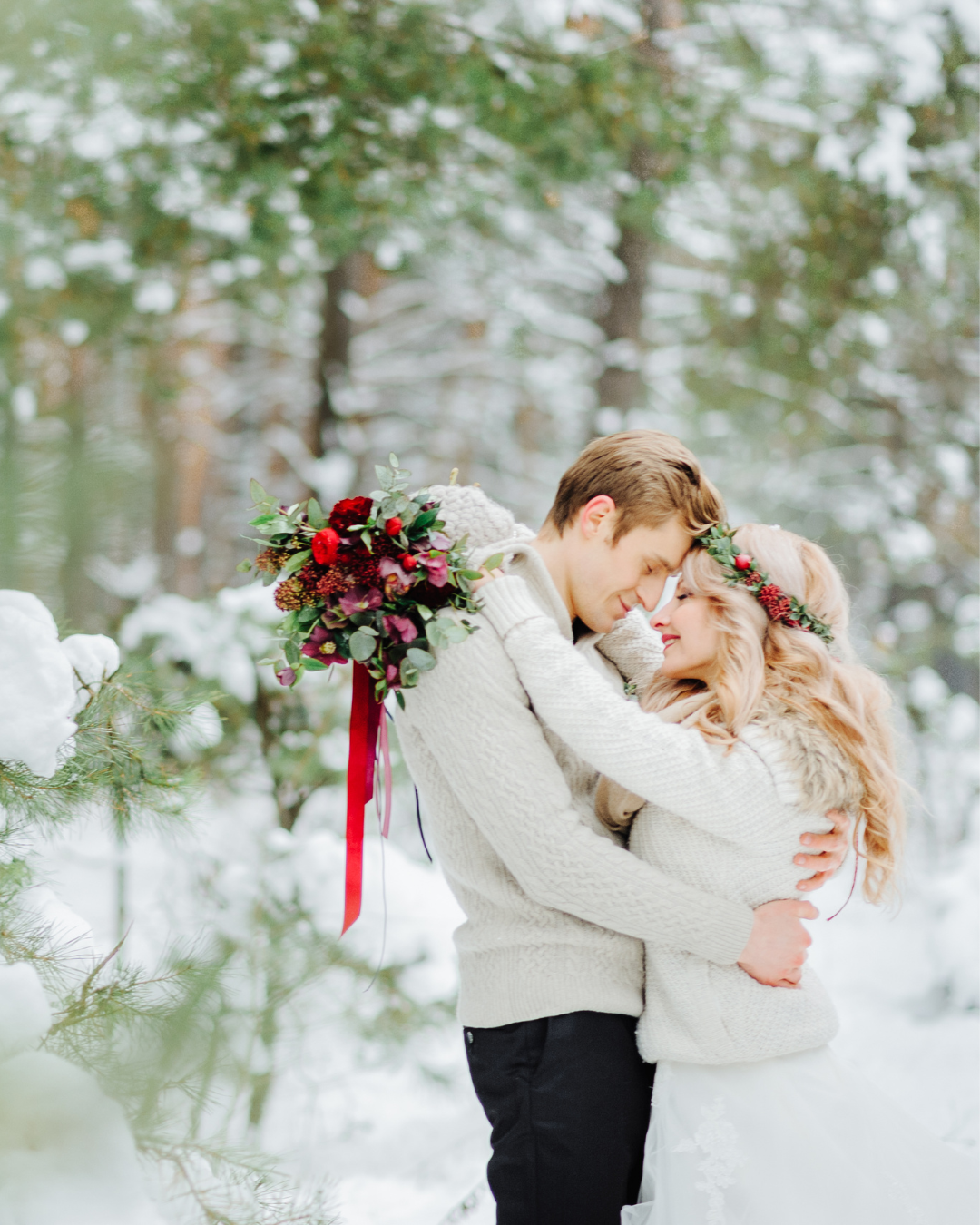 Braut und Bräutigam umarmen sich im verschneiten Wald, mit winterlichem Blumenstrauß in Bordeaux-Tönen.
