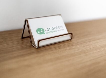 Visitenkartenhalter auf einem Holztisch mit einer Visitenkarte für eine Logopädie-Praxis, vor einem weißen Hintergrund: Das Schnatterwerk