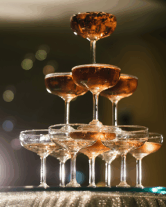 Sektgläser werden in Form einer Pyramide gestapelt, gefüllt mit rosafarbenem Sekt, mit unscharfem Hintergrund und warmem Licht.