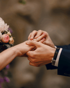 Hochzeitsmusik bei der Trauung: Nahaufnahme eines Paares bei der Ringübergabe während der Hochzeit, die Hände zeigen einen Ehering und einen Verlobungsring, im Hintergrund sind leichte Blumen zu sehen