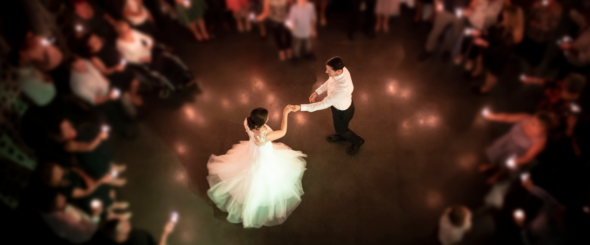 Hochzeitsmusik: Braut und Bräutigam tanzen in der Mitte eines Kreises von Gästen bei einer Hochzeit, aufgenommen von oben mit Fokus auf das Paar und verschwommenem Hintergrund.