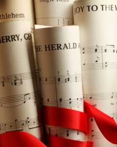 Historische Notenblätter mit roter Schleife – Weihnachtsmusik zwischen Tradition und kulturellem Wandel. Weihnachtsnoten mit roten Bändern, darunter "Joy to the World", "The Herald" und "Bethlehem".