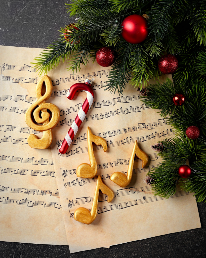 Weihnachtsnoten und Zuckerstange – 300 Jahre Weihnachtslieder im Wandel der Zeit - Weihnachtliche Dekoration mit goldenen Noten, einem Zuckerstangenornament, Notenblättern und Tannenzweigen mit roten Kugeln.