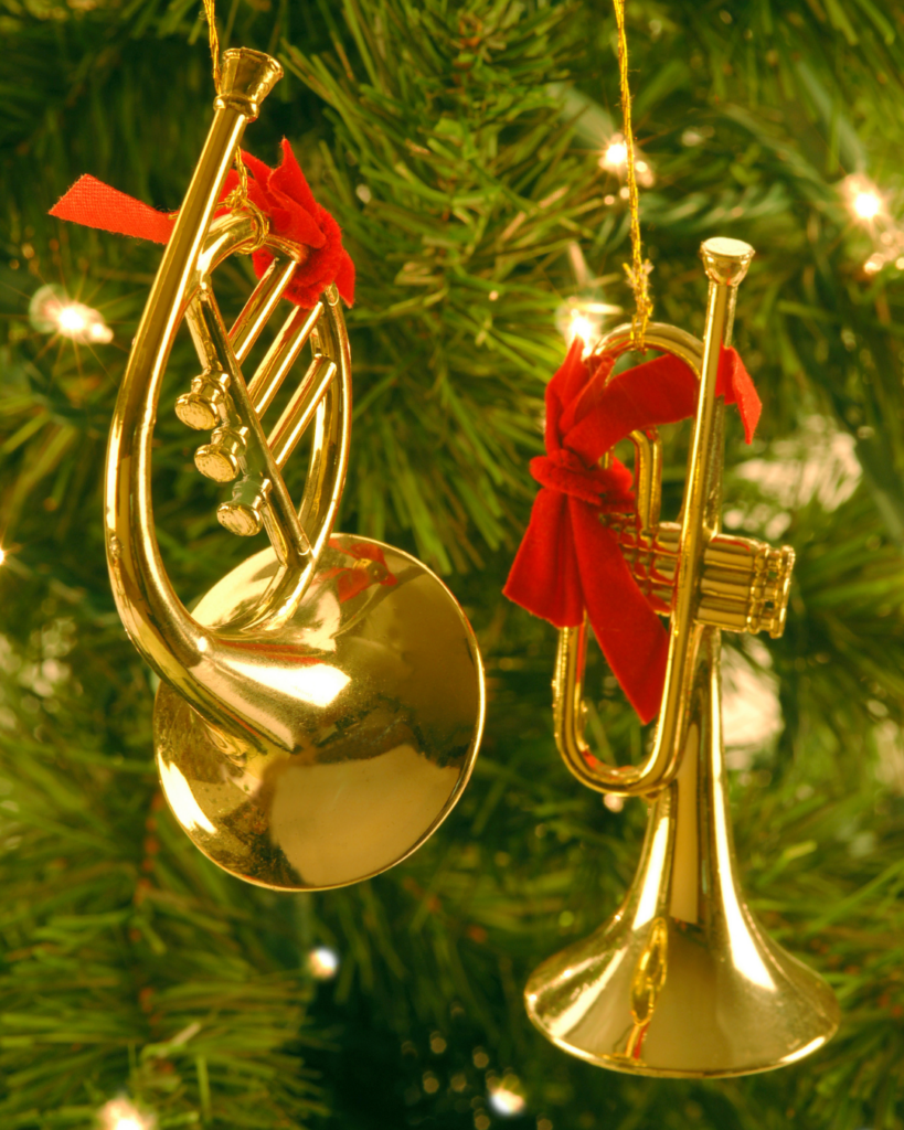 Goldene Trompeten am Weihnachtsbaum – bürgerliche Weihnachtsmusik im 19. Jahrhundert. Goldfarbene Weihnachtsbaum-Anhänger in Form einer Trompete und einer französischen Horn mit roten Schleifen an einem Tannenbaum.