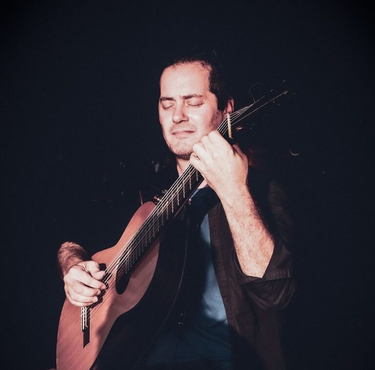 Mann mit geschlossenen Augen spielt Gitarre, dunkler Hintergrund, konzentrierter Gesichtsausdruck