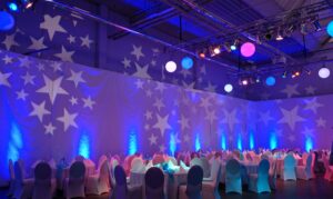 Festlich dekorierter Saal mit runden Tischen, weißen Stühlen und Sternenlichtprojektionen an den Wänden