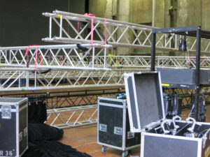 Aluminium-Traversen und mehrere schwarze Transportkoffer für Bühnentechnik in einer großen Lagerhalle.