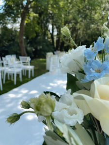 Nahaufnahme von weißen und hellblauen Blumen mit verschwommenen weißen Stühlen und einem weißen Gang im Hintergrund in einem grünen Garten
