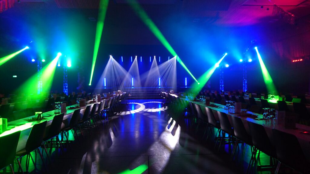 Großer Saal mit langem gedecktem Tisch und bunten Bühnenlichtern für ein Event oder eine Feier.
